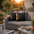 Set of 2 black vegan leather throw pillow covers styled on outdoor wicker sofa at sunset