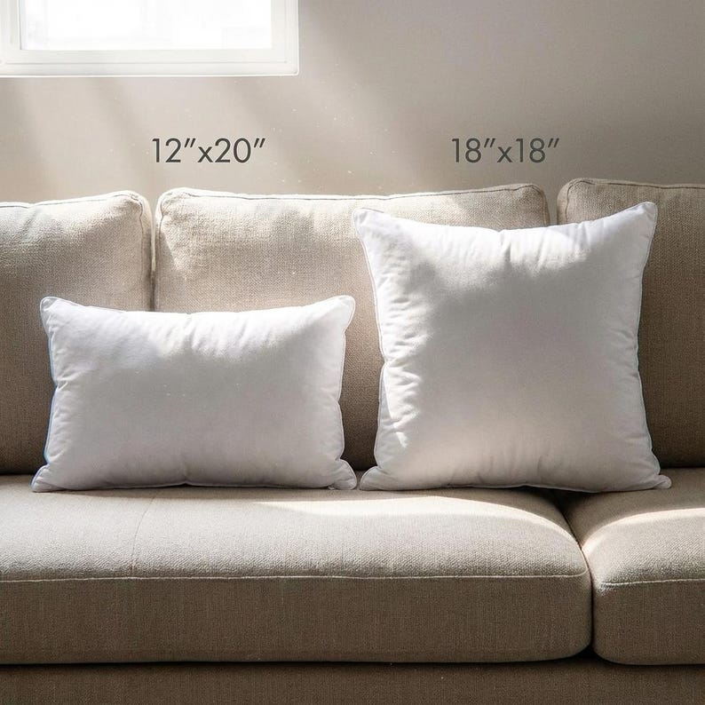 Two white down alternative pillow inserts, 12"x20" and 18"x18", on a beige couch by a window. Soft synthetic pillow options.
