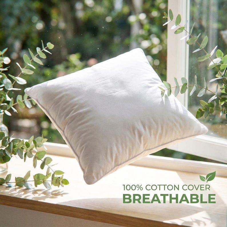 White down alternative pillow insert with 100% cotton cover, positioned on a sunlit windowsill surrounded by green...