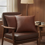 Two rich brown faux leather crocodile embossed pillows on a modern brown armchair in a warm living room setting with lamp...