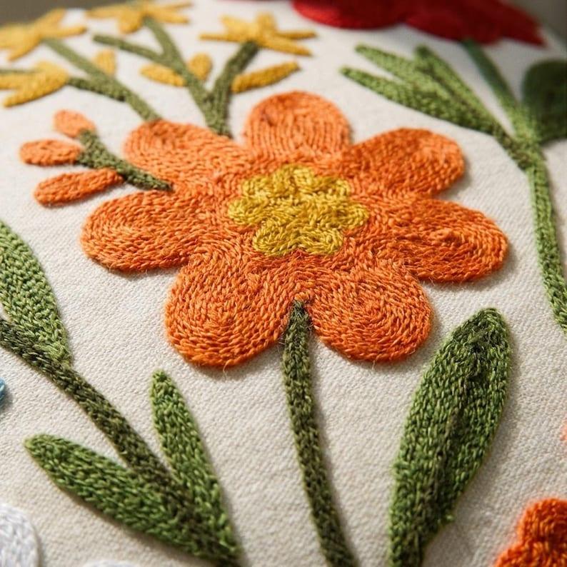 Close-up of wool thread embroidery detail on wildflower pillow cover — orange daisy with textured petals