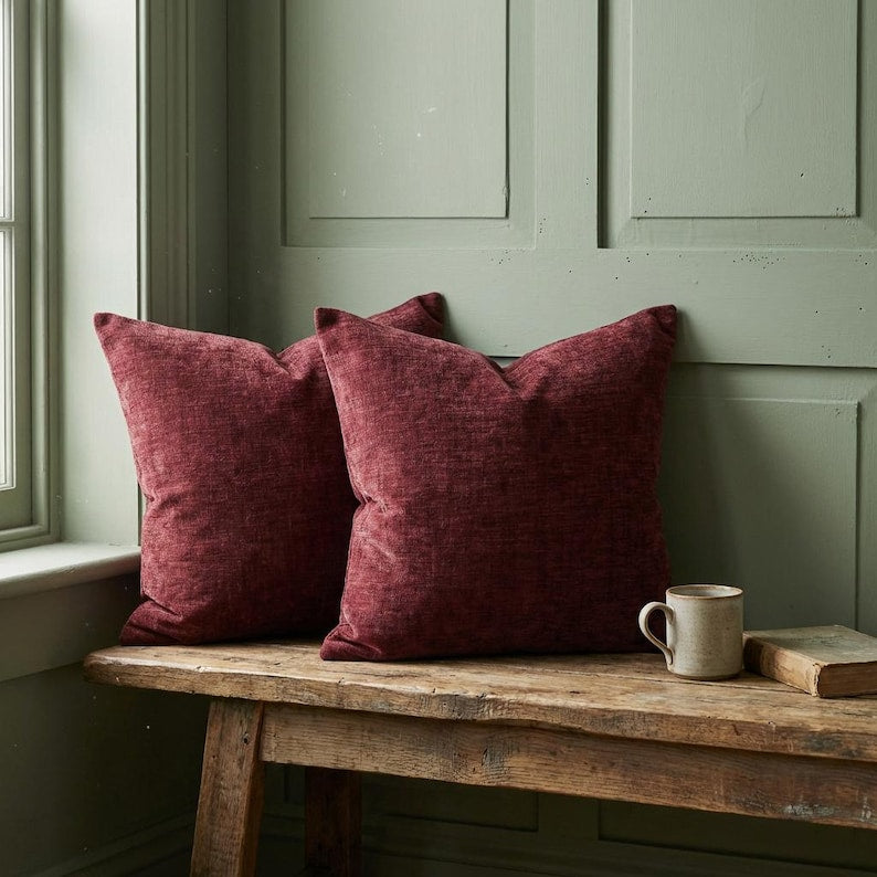 Two burgundy chenille pillow covers on a rustic wooden bench against a sage green wall, with a mug and book, for home decor.