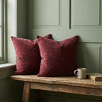 Two burgundy chenille pillow covers on a rustic wooden bench against a sage green wall, with a mug and book, for home decor.
