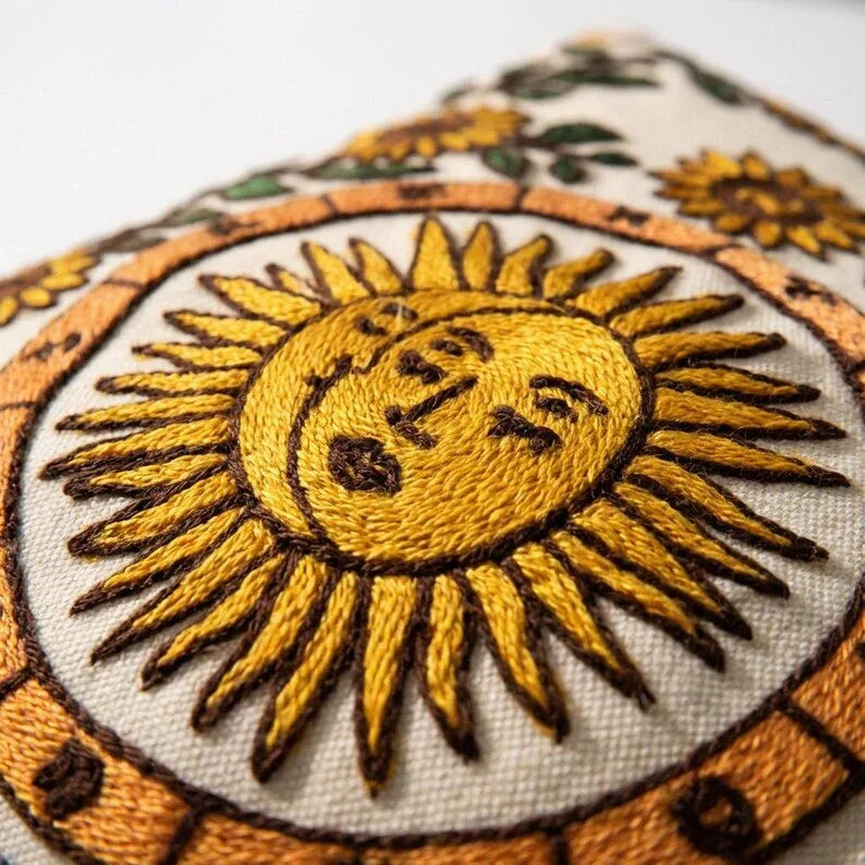 Close-up of chain-stitch embroidery detail — golden sun face and zodiac wheel on cotton canvas pillow cover
