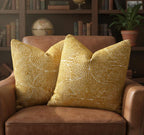 Two yellow patterned pillows on a brown leather chair with a bookshelf in the background.