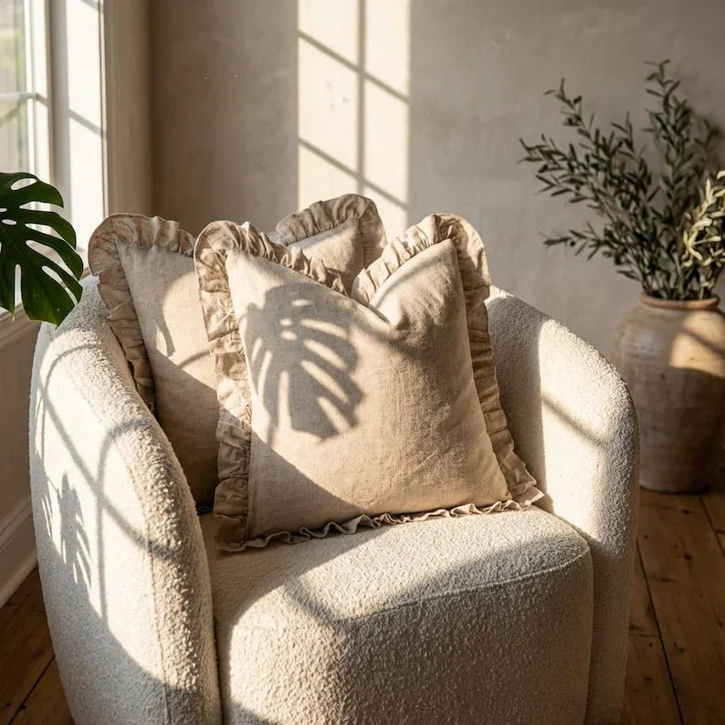 Two linen ruffle pillow covers styled on a boucle armchair in a bright living room