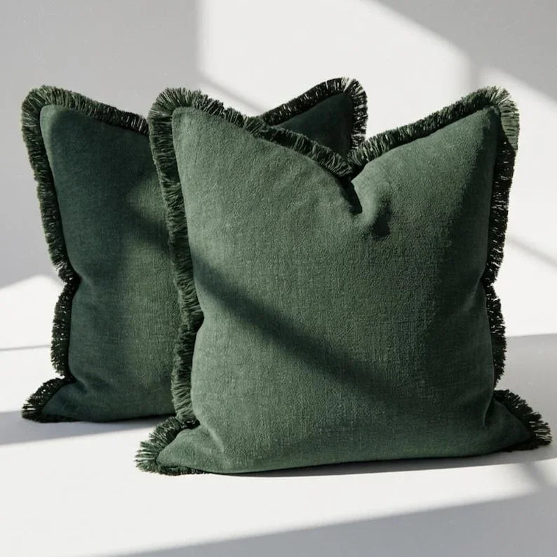 Set of 2 olive green linen throw pillow covers with fringe trim on all four sides, styled on a white surface