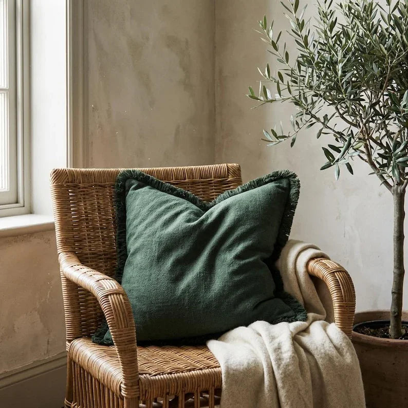 Olive green linen fringe pillow cover styled on a rattan accent chair beside an olive tree in a neutral organic interior