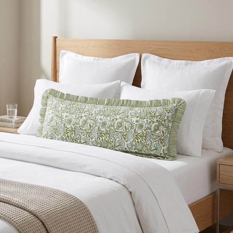 Handcrafted floral block print bolster pillow cover with ruffle trim on a bed with white bedding