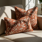 Chenille botanical pillow covers in burnt orange with sage green leaf motif, styled on linen sofa in natural light — square and lumbar sizes