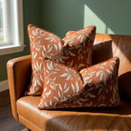Burnt orange botanical floral chenille pillow covers styled on tan leather sofa — square and lumbar sizes shown together