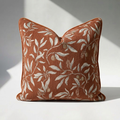 Luxury chenille throw pillow cover in burnt orange with botanical floral print, sage green leaf and fruit motif, self-piped edge — 18x18 square, close-up texture detail