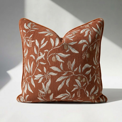 Luxury chenille throw pillow cover in burnt orange with botanical floral print, sage green leaf and fruit motif, self-piped edge — 18x18 square, close-up texture detail