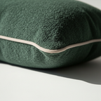 Corner detail of a dark green boucle pillow cover with light beige piping, highlighting the textured fabric and...