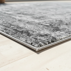 Corner close-up of gray distressed area rug showing low pile texture and non-slip backing edge on hardwood floor