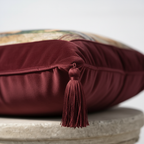 Side view of burgundy velvet pillow cover highlighting matching hand-tied corner tassel detail