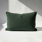 Rectangular dark green boucle pillow cover with beige piping, soft textured fabric on white background, natural light.